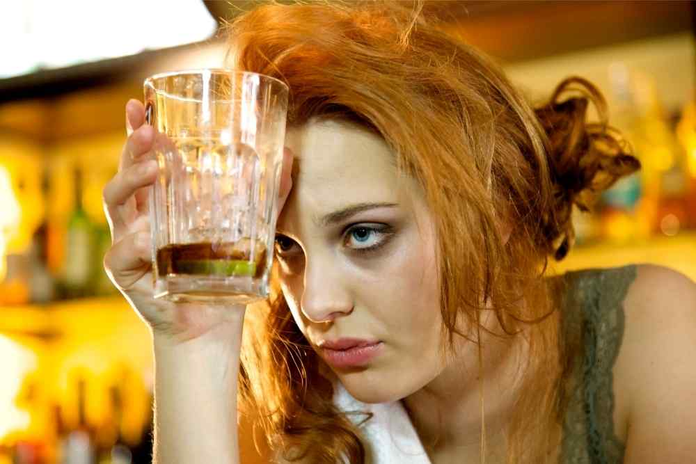 woman holding glass to forehead hungover