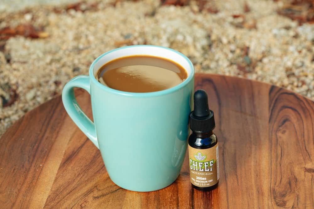 cbd oil next to a steaming mug of joe