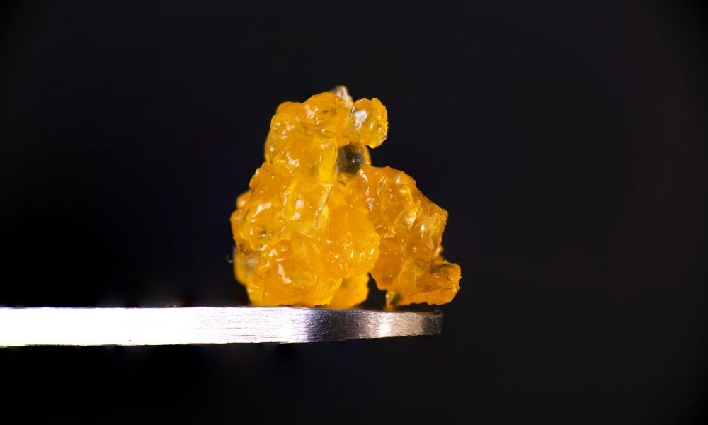 a ball of amber cbd distillate sitting on a nail against a black background