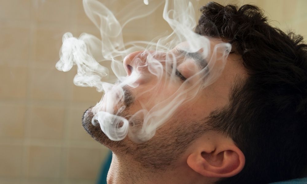 man exhaling cloud of smoke