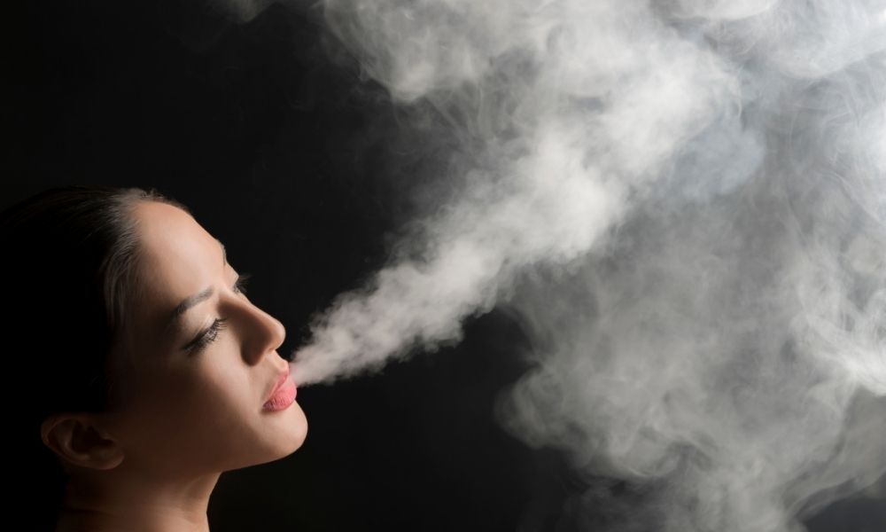 woman exhaling vapor against black background