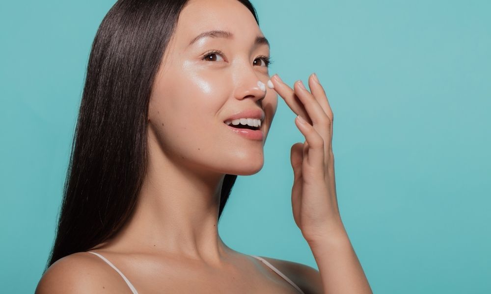 young woman applying moisturizer to nose