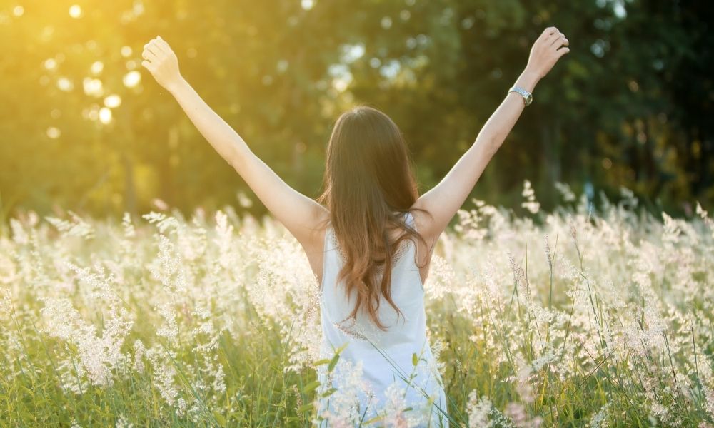 a girl in a white dress standing in a grassy field with her arms up because she ordered free cbd samples