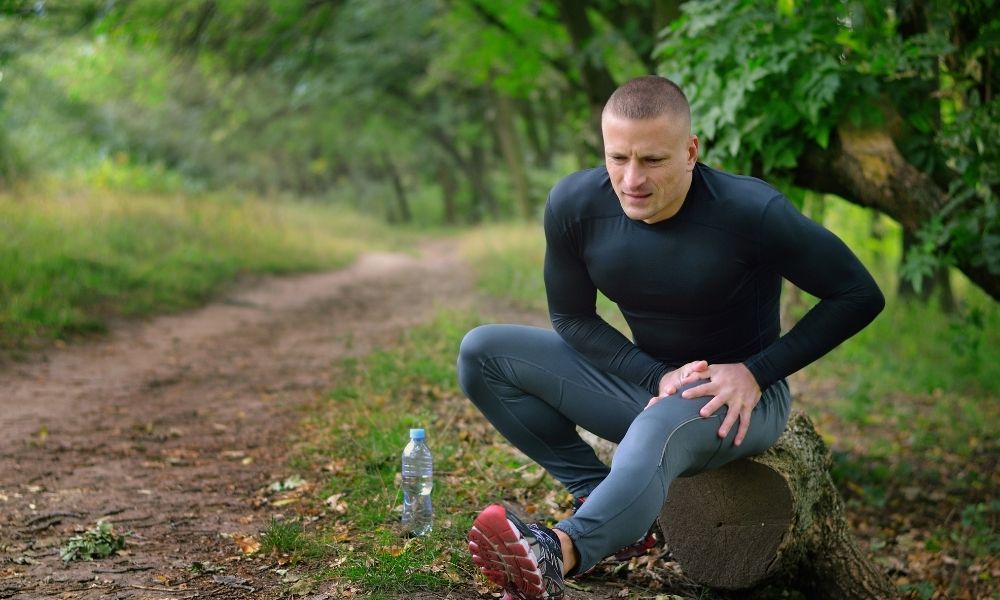 young male exercising on an outdoor trail with a leg cramp