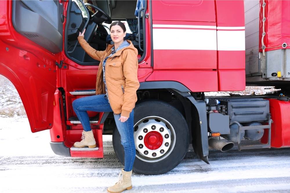 female truck driver posing by red truck