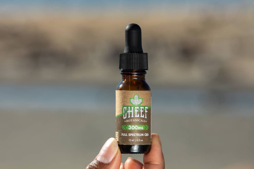 holding up cbd oil against beach background