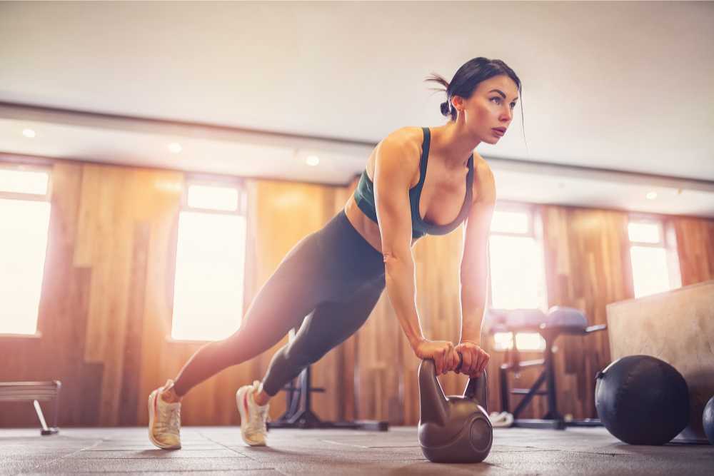 focused woman planking on kettlebell