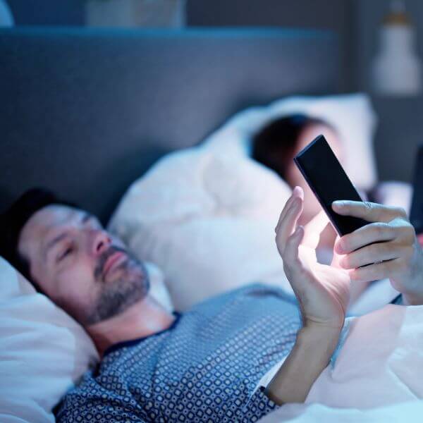 man laying in bed at night looking at phone screen 