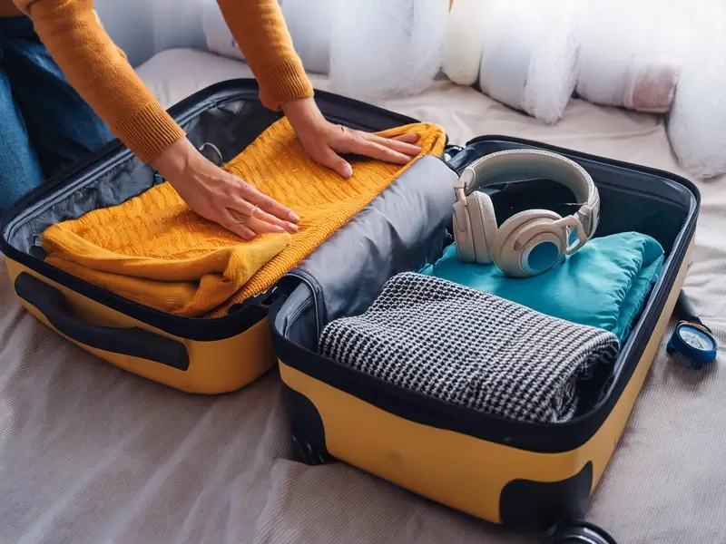 a person's hands packing a suitcase. In the suitcase is noise canceling headphones